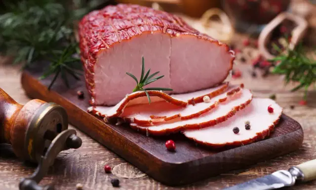 Pokrojona szynka wieprzowa z rozmarynem i pieprzem na desce.