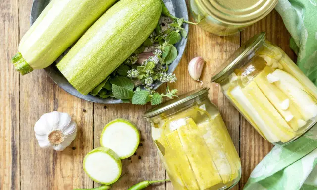 Zucchini haltbar machen: Frische Zucchini, Knoblauch, Chili und Kräuter für die Konservierung in Gläsern.
