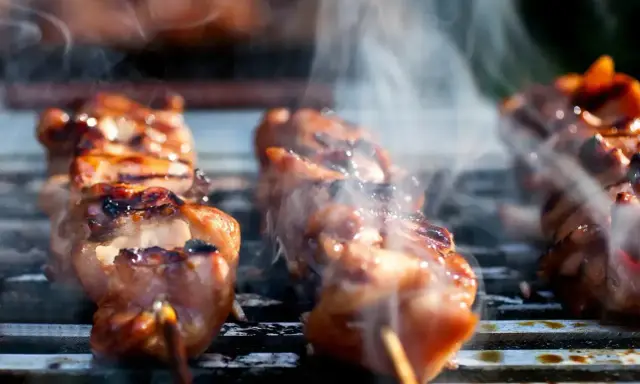 Aromatyczne yakitori skwierczy na grillu, otoczone kłębuszkami dymu.