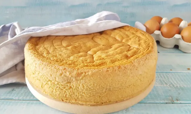 Un soffice pan di spagna dorato, coperto da un canovaccio, con uova fresche sullo sfondo.