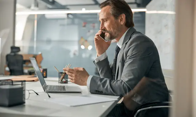 Mężczyzna w garniturze rozmawia przez telefon, pracując przy laptopie. To typowy dzień w pracy, nawet dla samego CEO.