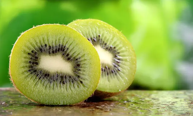 Dwa soczyste kiwi, przekrojone na pół, ukazują swoje zielone wnętrze z czarnymi pestkami. To naturalne kiwi co leczy, pełne witamin.