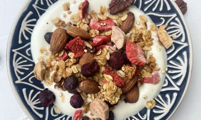 Schüssel mit Joghurt, garniert mit knusprigem Müsli, Mandeln, gefriergetrockneten Erdbeeren und Blaubeeren. Perfekt für gesunde Frühstücks-Granola-Rezepte.