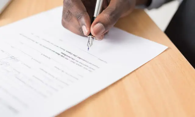 Mano firmando un documento, cumpliendo con el artículo 6 de la LAU, que requiere aprobación para la compra.