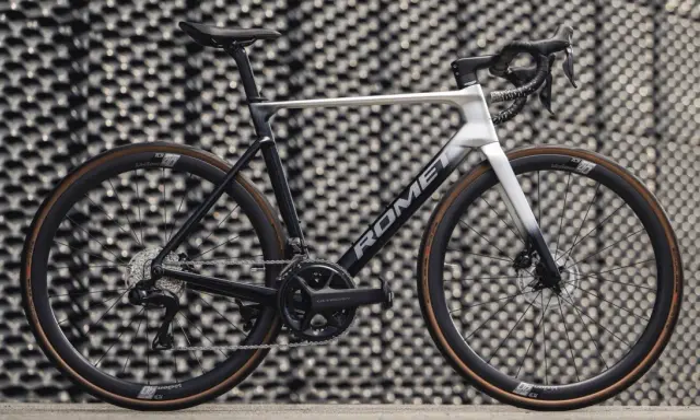 Nowoczesny rower szosowy marki Romet z osprzętem Shimano Ultegra, prezentujący się na tle geometrycznej ściany.
