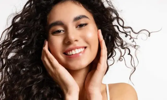 Sonrisa radiante con un toque de strawberry makeup, cabello rizado oscuro y piel luminosa.