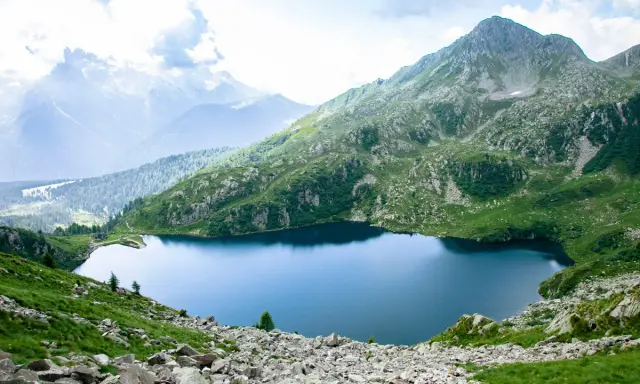 Un sereno lago ritorto incastonato tra montagne verdi e rocciose, con cime nebbiose all'orizzonte.