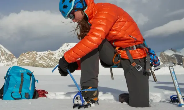 Alpinistka przygotowuje raki automatyczne lub półautomatyczne do wspinaczki. W tle góry.