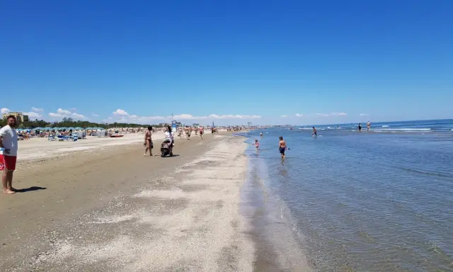 Una giornata di sole a Pinarella di Cervia mare, con bagnanti che passeggiano sulla sabbia e bambini che giocano nell'acqua cristallina.