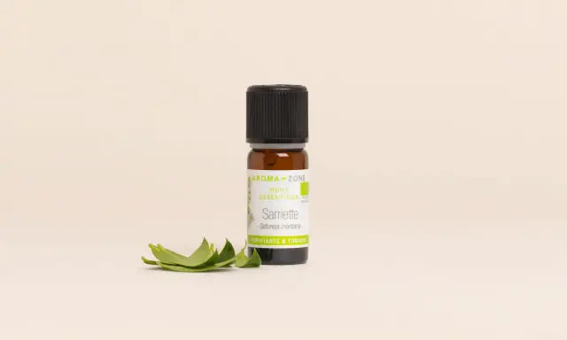 Flacon d'huile essentielle sarriette des montagnes, aux vertus purifiantes et toniques, accompagné de quelques feuilles fraîches.