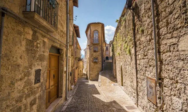 Antica scala di borgo in pietra, con case strette e un cielo azzurro.