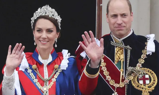 Kate Middleton och Prins William, medlemmar av brittiska kungahuset, vinkar från en balkong i sina högtidliga dräkter och juveler.