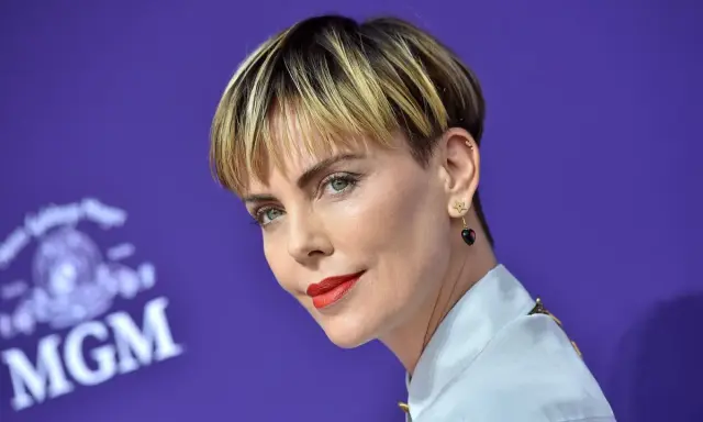 Charlize Theron mit fransigen Kurzhaarfrisuren Damen, rotem Lippenstift und Stern-Herz-Ohrringen vor MGM-Logo.