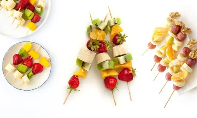 Brochetas de frutas coloridas con fresas, kiwi, plátano, mango, naranja, uvas y nueces. ¡Un postre refrescante y saludable!