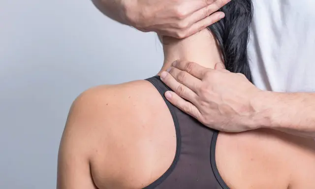 Hände eines Therapeuten untersuchen den Nacken einer Frau, um schmerzen seitlich am Hals entlang zu lindern.