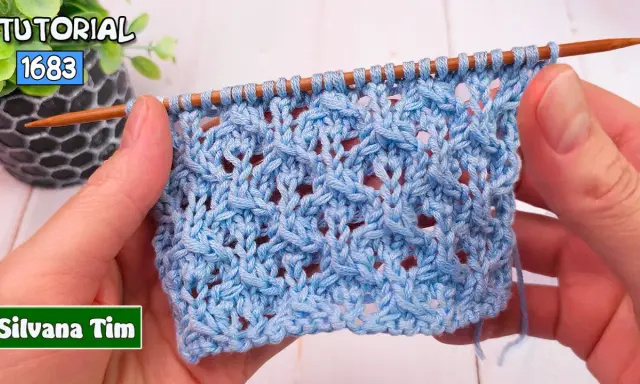 Manos tejiendo un patrón de puntos calados a dos agujas utilisima en hilo azul claro. El tejido muestra un diseño intrincado con agujeros y trenzas.