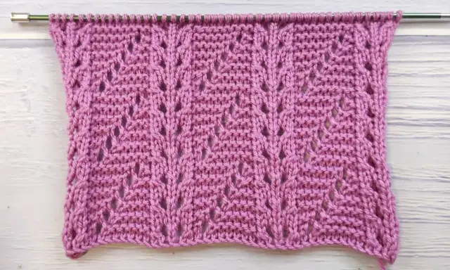 Muestra de tejido con puntos fantasía crochet en color rosa, con un patrón de hojas caladas.