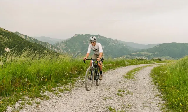 Kolarz na rowerze pokonuje krętą drogę z **gravel co to** w tle górskiego krajobrazu.
