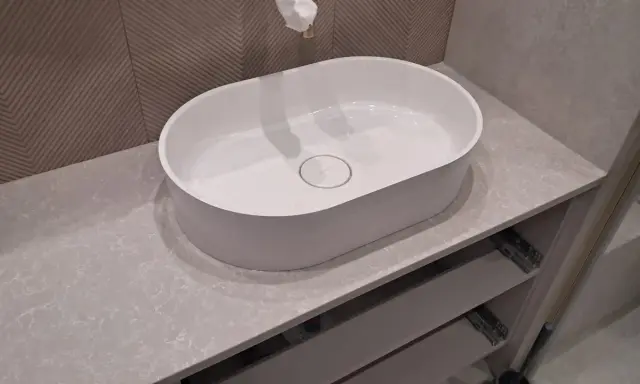 Elegancka łazienka z owalną umywalką nablatową na blacie z konglomeratu kwarcowego. Jasne, subtelne kolory kamienia tworzą spokojną atmosferę.