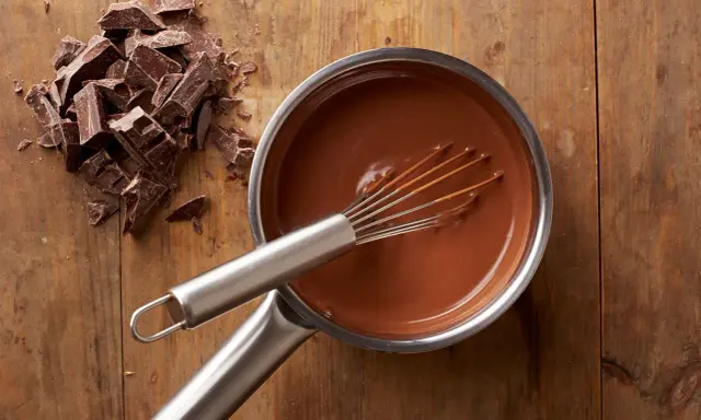 Chocolat fondu qui durcit dans une casserole, avec des morceaux de chocolat à côté sur une planche en bois.