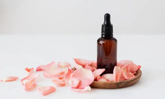 Flacon d'huile essentielle ambré entouré de pétales de rose. Un soin doux pour une femme enceinte.