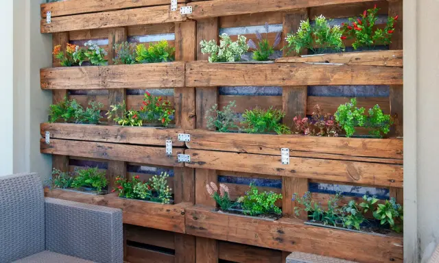 Un **jardín vertical con palets** luce plantas verdes y rojas en un diseño rústico.