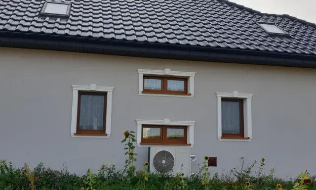 Elegancki gzyms co to? Ozdobne obramowanie okien na szarym domu z brązowymi oknami i słonecznikami.