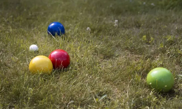 Boules colorées (jaune, rouge, bleu, vert) et une petite blanche sur l'herbe, prêtes pour un concours de pétanque.