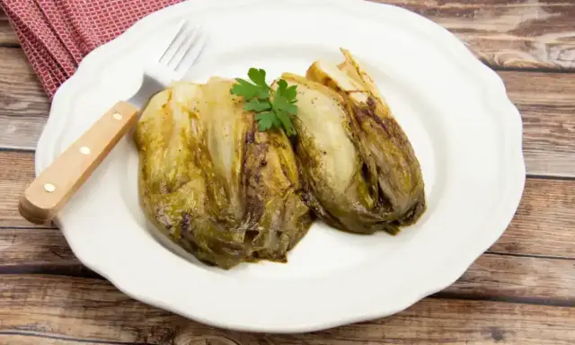 Deux endives caramélisées à la poêle, garnies de persil, sur une assiette blanche avec une serviette à carreaux rouges et une fourchette.