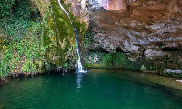 La cascada del río Carbo cae en una poza de agua verde esmeralda, rodeada de rocas cubiertas de musgo y vegetación exuberante.