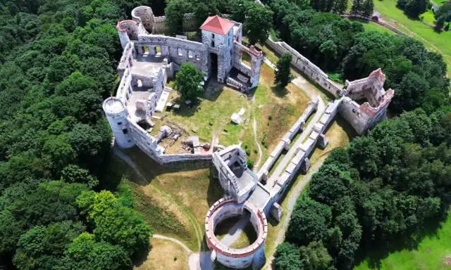 Zamek Rudno, otoczony bujną zielenią, prezentuje się jako malownicza ruina z kamiennymi murami i wieżami.