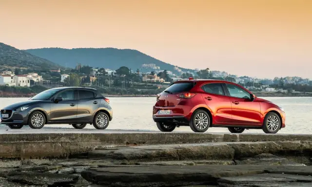 Dos Mazda, uno gris y otro rojo, junto al mar. La fiabilidad Mazda se refleja en su diseño y presencia.