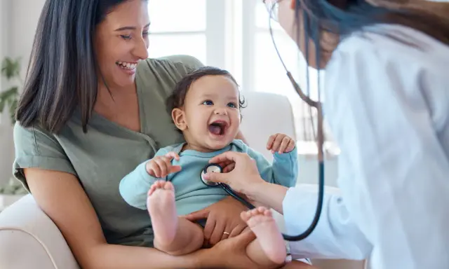 Glad mamma ser sitt barn få ett års vaccin. Läkaren lyssnar på barnets hjärta med stetoskop.