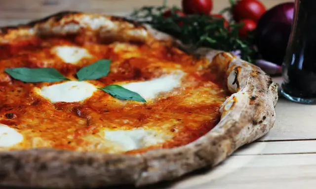 En perfekt pizza på grillen, med smält mozzarella och färsk basilika. Tomater och vitlök i bakgrunden.