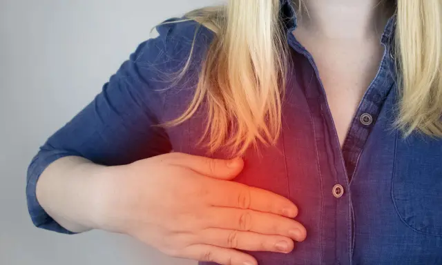 Kobieta z ręką na piersi, gdzie widoczny jest czerwony obszar bólu. Szuka informacji o lekach na torbiele w piersiach.