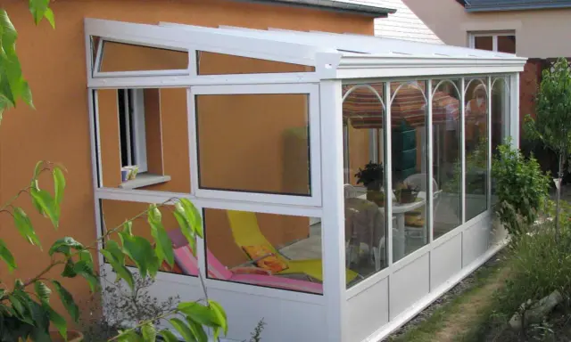 Une véranda démontable sans permis de construire, avec chaises longues et table à manger, prolonge la maison pour profiter du jardin.