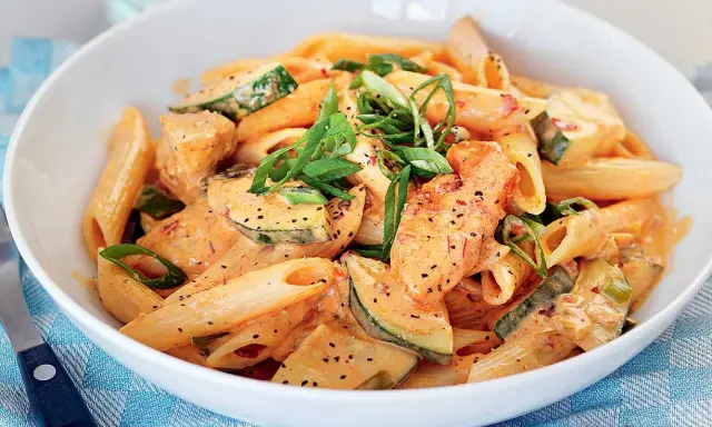 En skål med krämig penne med kyckling och zucchini, toppad med salladslök. En riktigt god pasta!