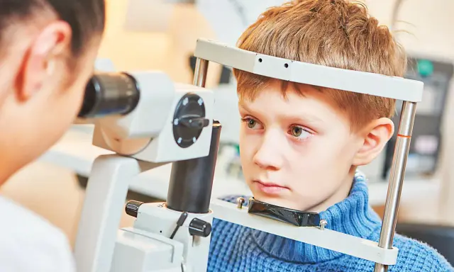 Chłopiec przechodzi komputerowe badanie wzroku u dzieci. Okulista bada jego oczy za pomocą specjalistycznego sprzętu.