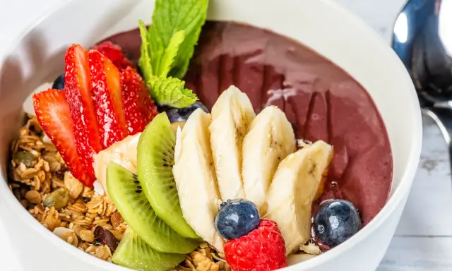 Acai-Schüssel mit Früchten, Granola und einem Hauch von Vitamin C. Erdbeeren, Bananen, Kiwi, Blaubeeren und Himbeeren machen diese Schüssel zu einem gesunden Genuss.