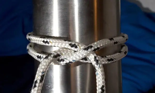 Un nœud pare battage, simple et efficace, sécurise une corde blanche et noire autour d'un mât métallique.