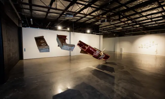 Suspended sculptures of weathered wood and metal hang in the spacious praxis gallery, casting long shadows on the concrete floor.