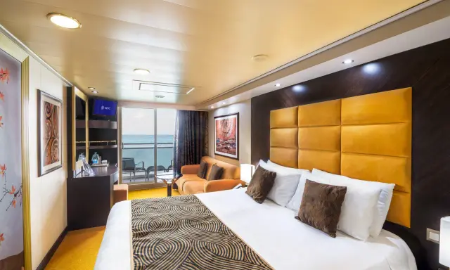 Interno di una cabina con balcone MSC Splendida: letto king-size, divano arancione, TV e vista mare.