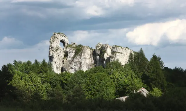 Imponujący okiennik wielki, skalna brama wśród zieleni, z ukrytą chatką.