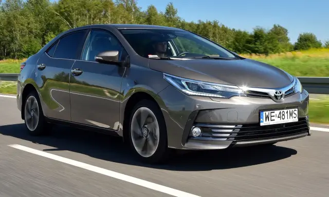 Szara Toyota Corolla E16 jedzie po drodze, za kierownicą siedzi mężczyzna.