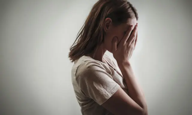 Kobieta zakrywa twarz dłońmi, co może symbolizować różne psychozy objawy, takie jak przytłoczenie czy izolacja.