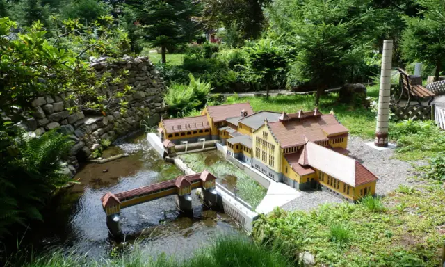Miniaturowa zabudowa z mostkiem i rzeką, jak w parkach miniatur w Polsce.