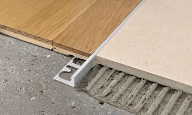 Un battiscopa metallico crea abbinamenti quando mancano le piastrelle del pavimento, unendo legno e ceramica su un sottofondo grezzo.