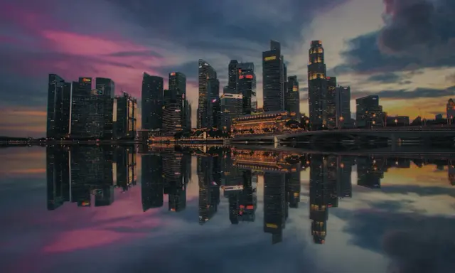 Wieżowce w Singapurze odbijają się w wodzie o zachodzie słońca. To miasto-państwo, gdzie leży Singapur, zachwyca nowoczesną architekturą.