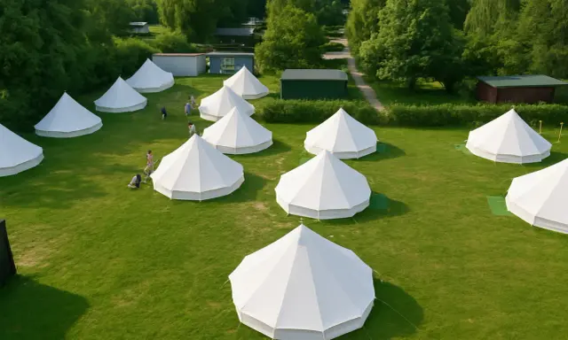 Wioska namiotów typu bell, idealna na glamping. Kilka osób spaceruje po zielonej trawie między białymi, stożkowymi konstrukcjami.