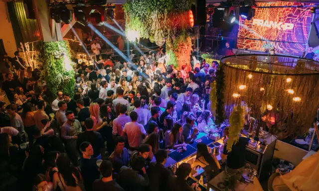 Menschen tanzen und feiern in einem belebten Club in Lissabon. Grüne Pflanzen und Lichter schaffen eine lebendige Atmosphäre.